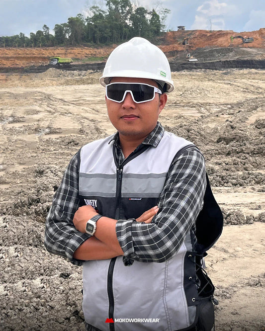 Construction worker wearing white hard hat, sunglasses, and safety vest at a mining site